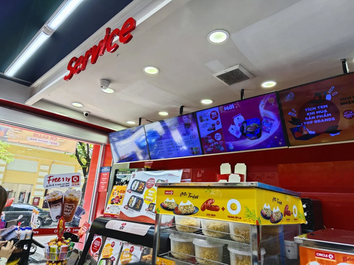 Circle K service counter in Vietnam with a row of digital menu and promotion screens