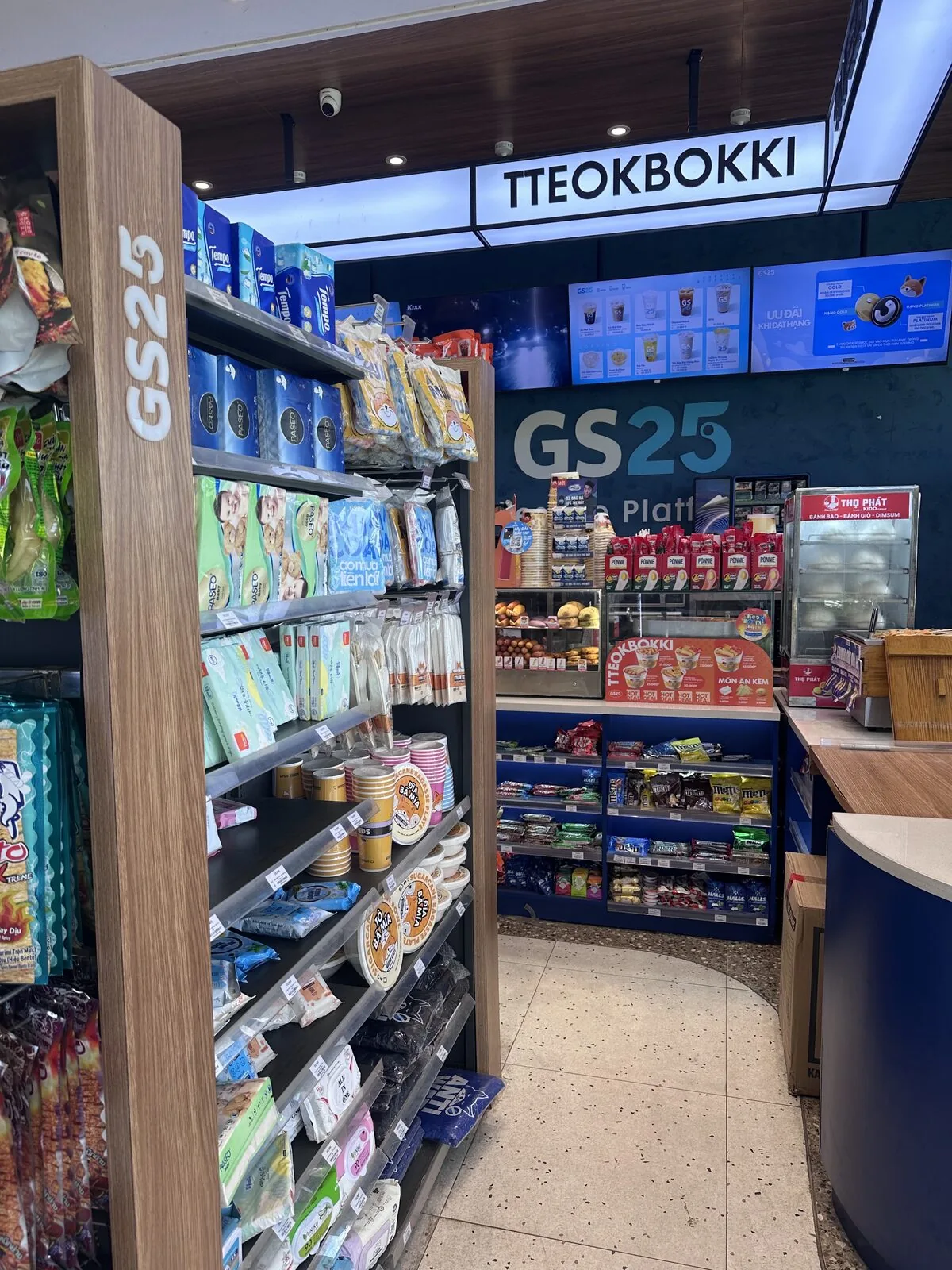 GS25 store interior in Vietnam with digital menu screens under the Tteokbokki sign